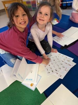 Two children placing yoga pose stickers into chakra-colored tracking books during a Grounded Kids Yoga class