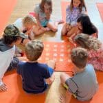 A group of homeschool children play a Grounded Kids Yoga memory game on orange mats, practicing focus and visual recall as part of a movement-based learning session