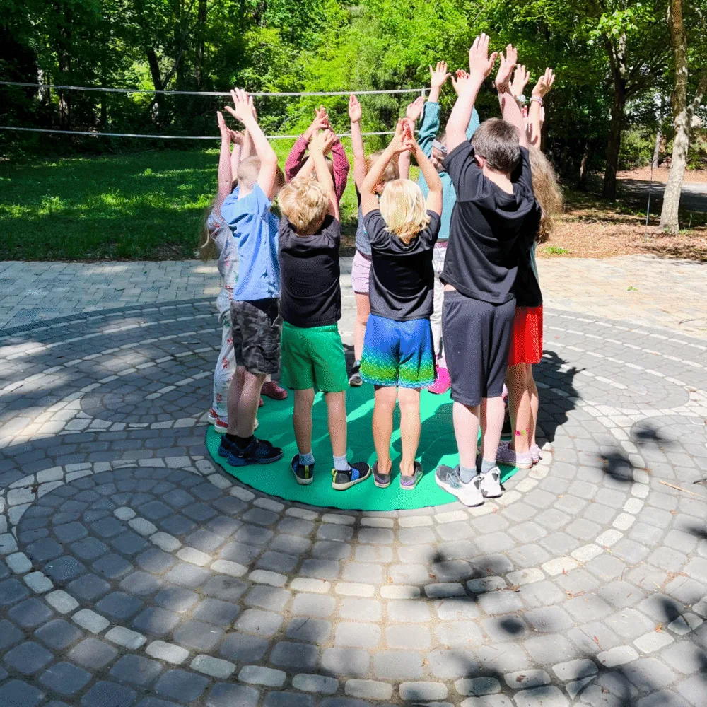Children standing in a circle during a group yoga pose with arms raised in a Grounded Kids Yoga session