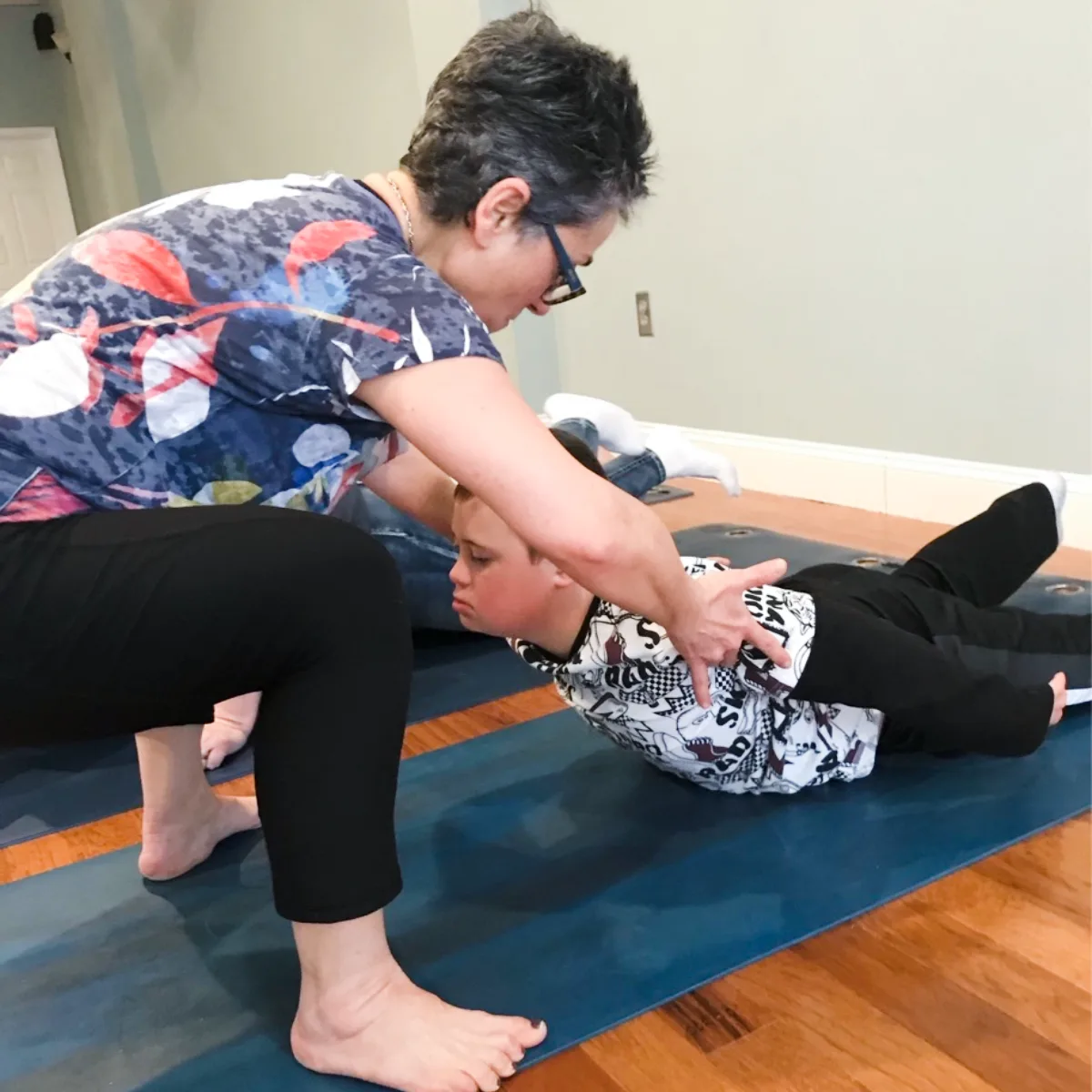 Adult guiding a neurodiverse child in yoga during a Grounded Kids Yoga session, offering hands-on support and calm encouragement in a studio setting