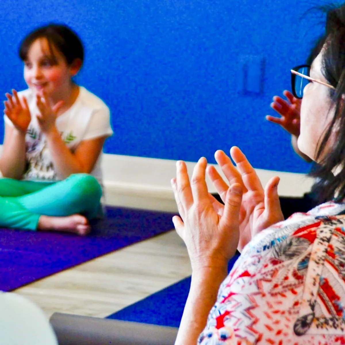 Instructor leading a Step 1 kids yoga teacher training session with a child on a yoga mat in a calm classroom environment