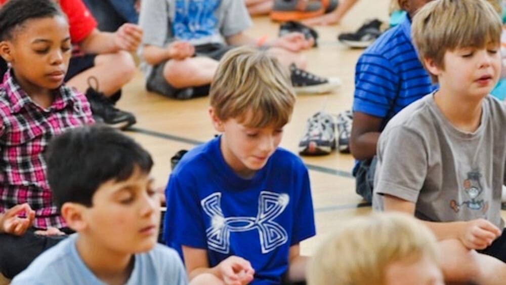 Children sitting in a group yoga class practicing mindfulness with eyes closed and hands in mudra