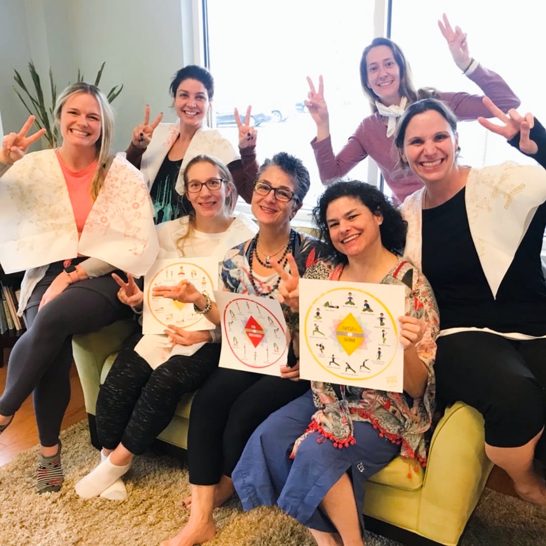 Group of kids yoga teacher trainees smiling and holding chakra posters during Step 2 Expand Your Reach certification with Grounded Kids Yoga