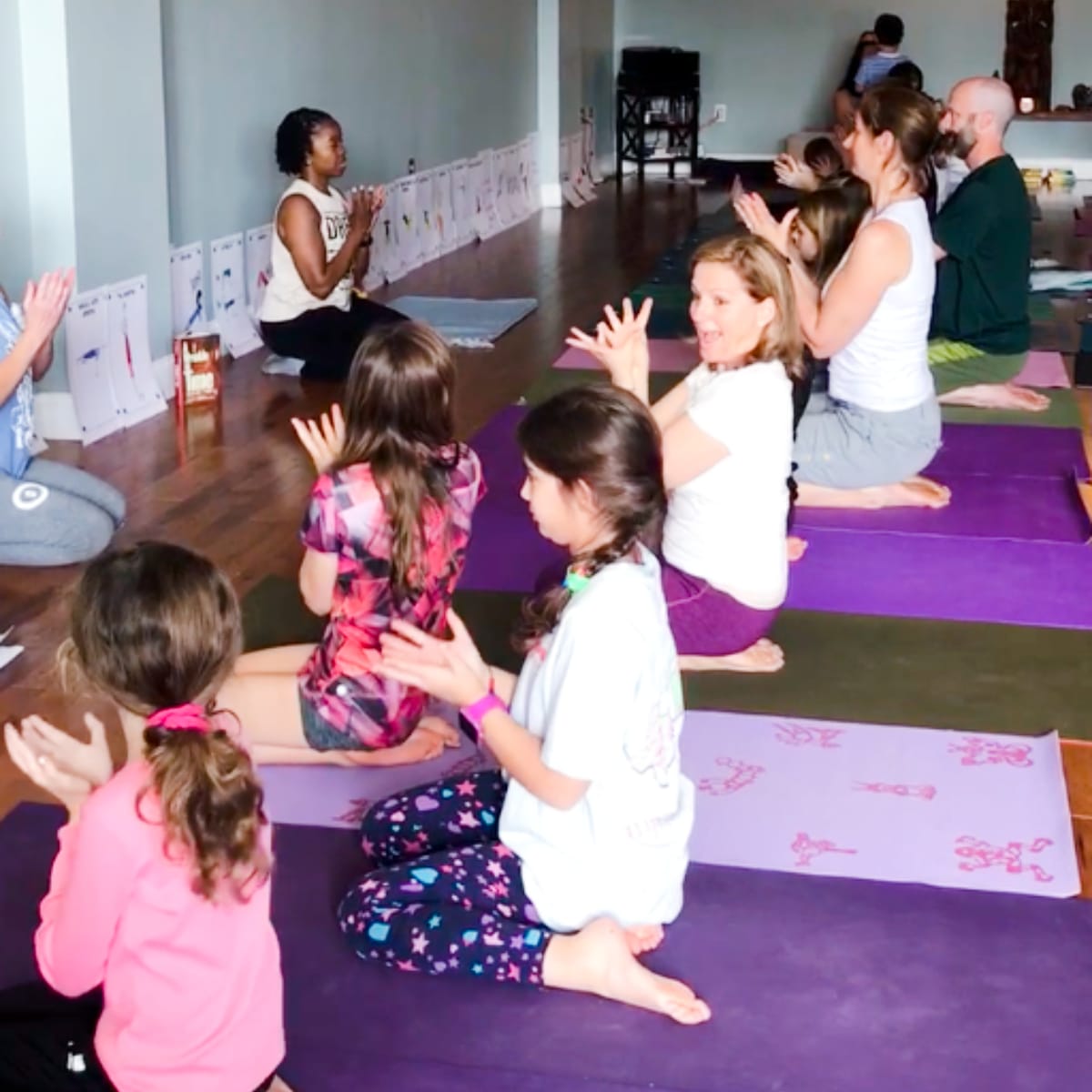 Kids yoga teacher leads a group of children and adults practicing together in a studio during Step 3 training