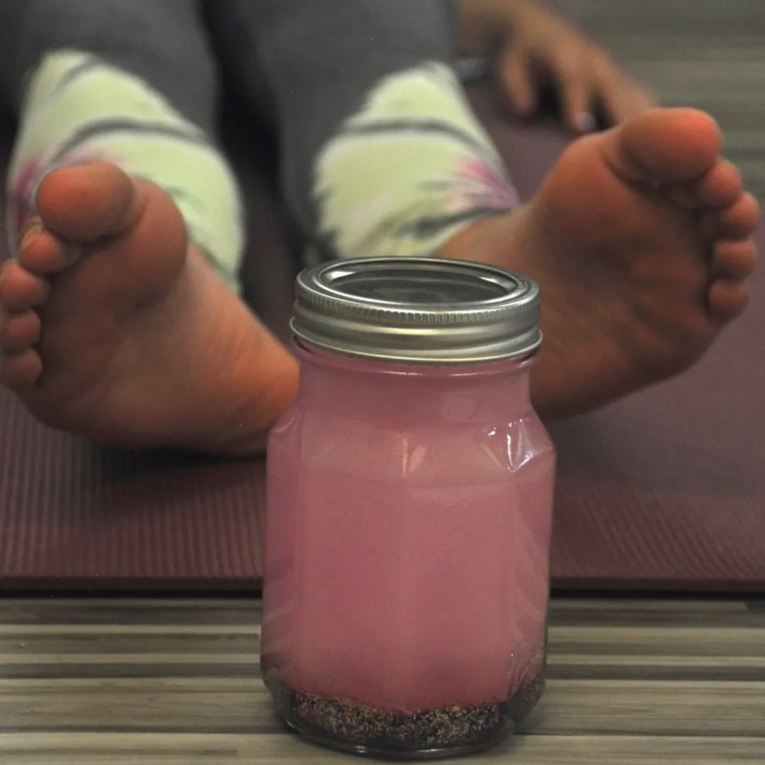 A pink Settle Down Jar sits on a yoga mat in front of a child lying down with bare feet visible in the background.