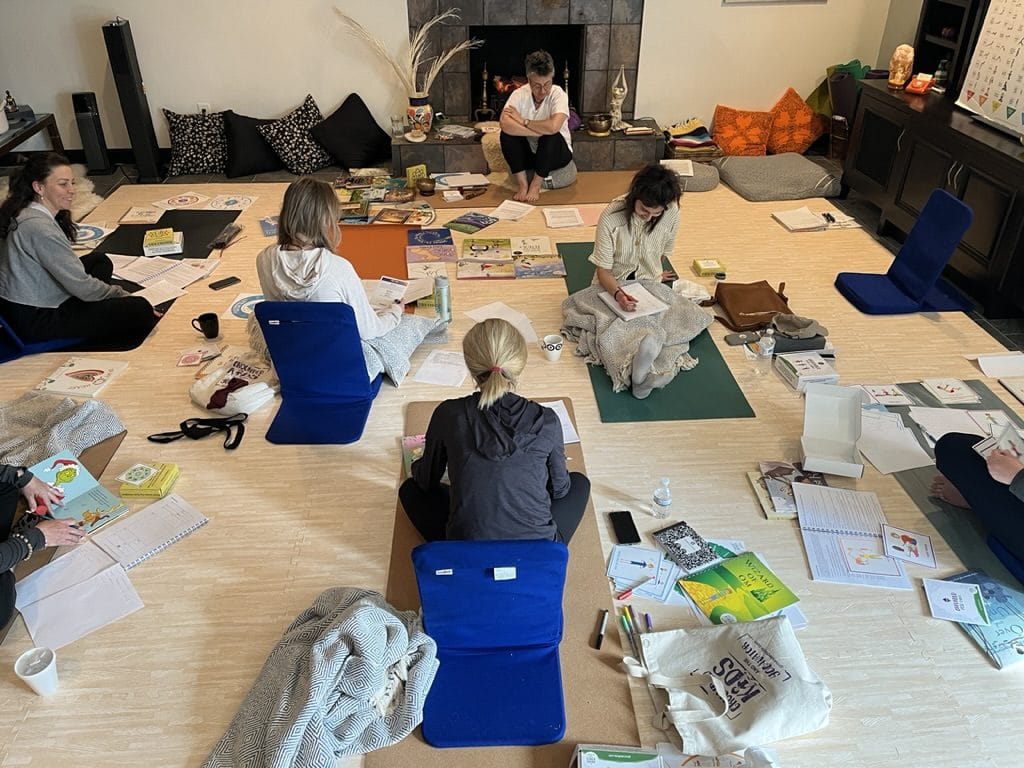 Six adults sit on the floor around yoga mats and open children's books during an in-person Grounded Kids yoga teacher training in Alpharetta, Georgia.