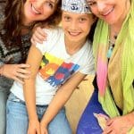 Charlotte, a Certified Grounded Kid, kneeling on a studio floor between Cheryl and Amy Haysman, all three smiling
