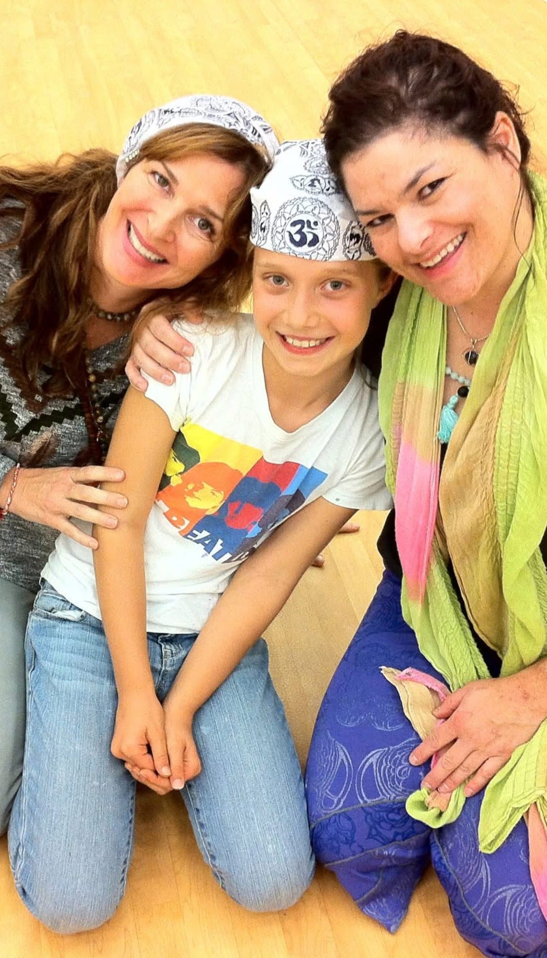 Charlotte, a Certified Grounded Kid, kneeling on a studio floor between Cheryl and Amy Haysman, all three smiling