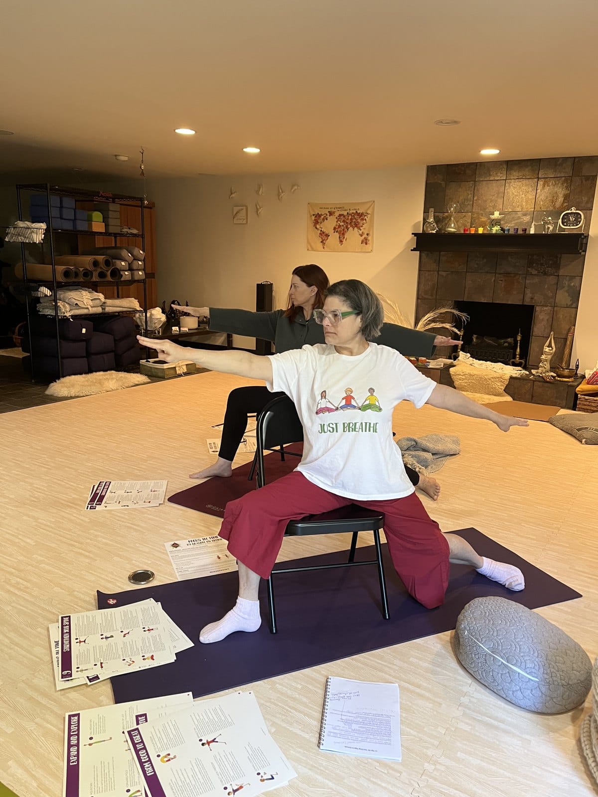 Grounded Kids founder Amy in a Just Breathe t-shirt practicing a chair yoga warrior 2 with Focus in Time sequence sheets spread on the floor in front of her