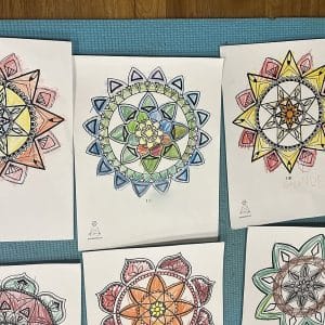 Six mandala pages from the I Am Centered Mandala Coloring Book, colored by kids in a Grounded Kids class, laid out on a teal yoga mat with "I Am" statements such as grounded, fun and joyful written under the designs.