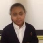 Fourth grade girl in a dark cardigan speaking to the camera, a still from the I Am What I Am video