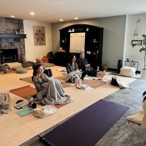 Grounded Kids lead trainer Sedef teaching Step 2 online and in person, with trainees seated on yoga mats under blankets in the studio.