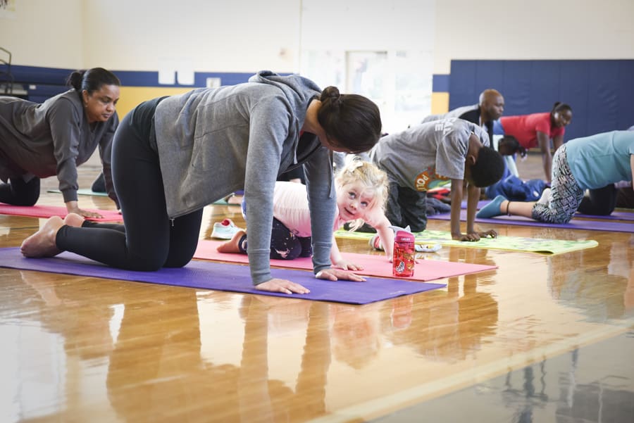Adults and children on hands and knees on yoga mats in a school gym