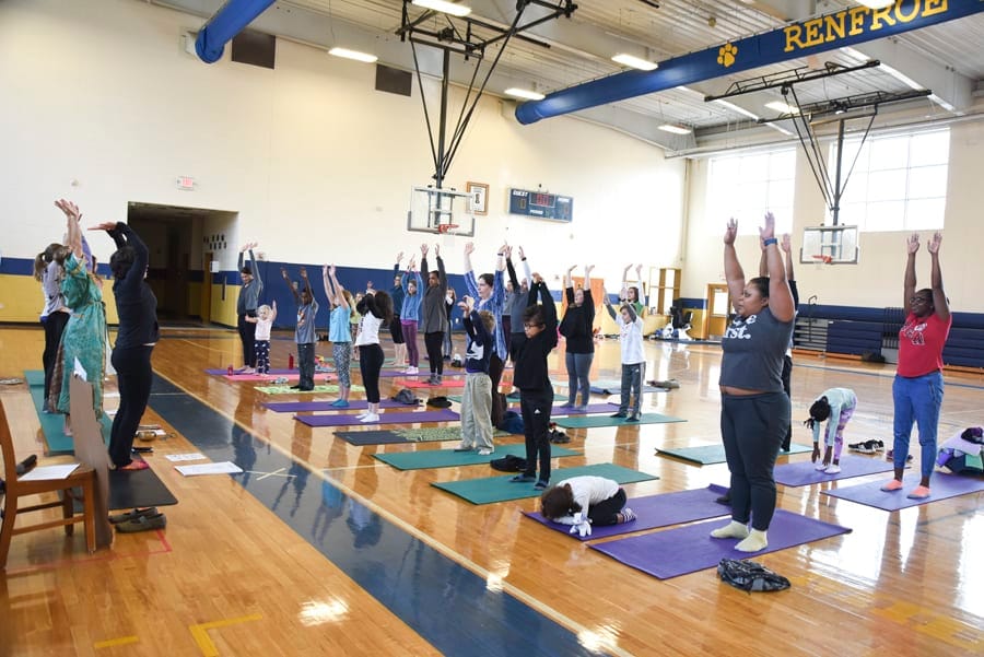 Families raising their arms overhead on yoga mats in a school gym