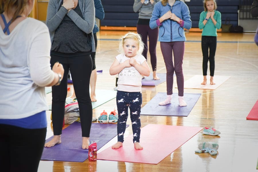 Young girl standing in Mountain Pose with hands at her heart among adults on mats