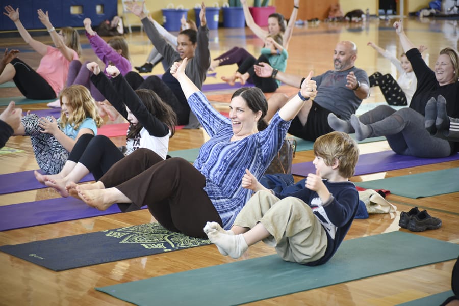 Adults and children laughing as they balance seated with legs lifted and one arm raised