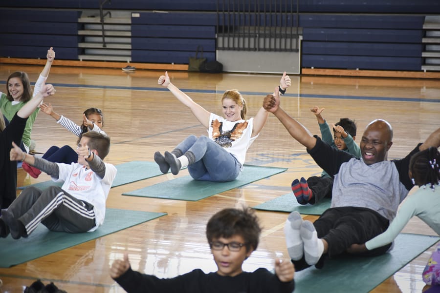 Adults and children balancing seated on yoga mats with arms raised, smiling