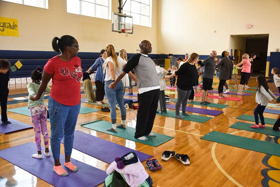 Adults and children standing and talking on yoga mats in a school gym