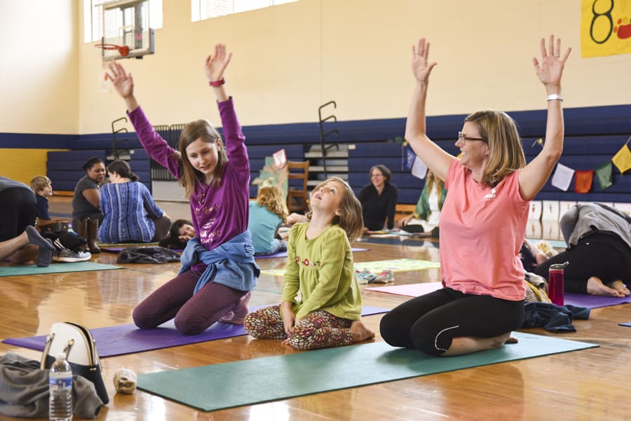 Girls and a woman kneeling on yoga mats with arms raised overhead