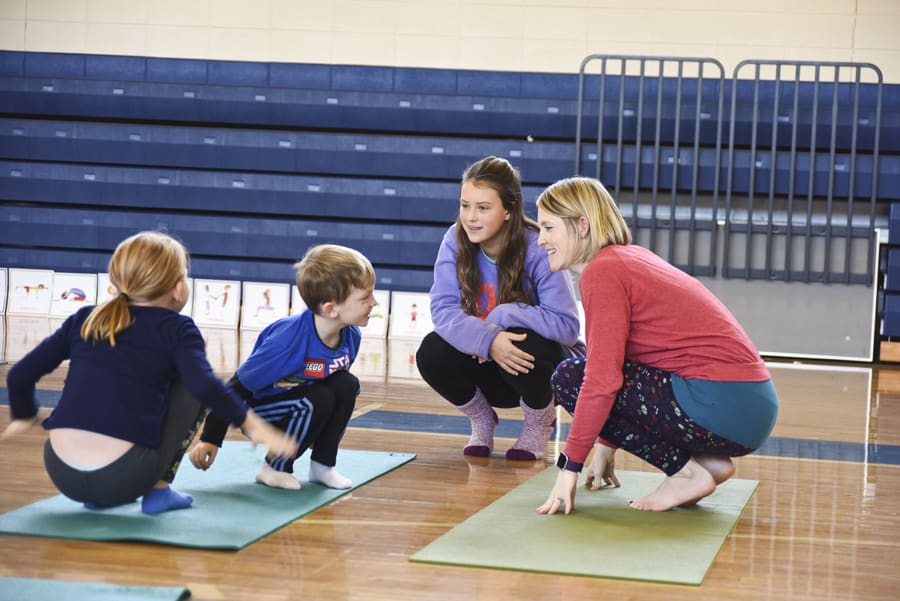 Woman and children squatting together on yoga mats in a school gym