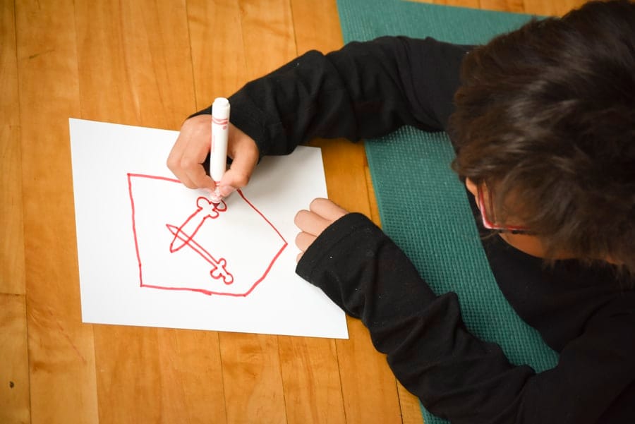 Child drawing a sword inside a shield outline for a coat of arms