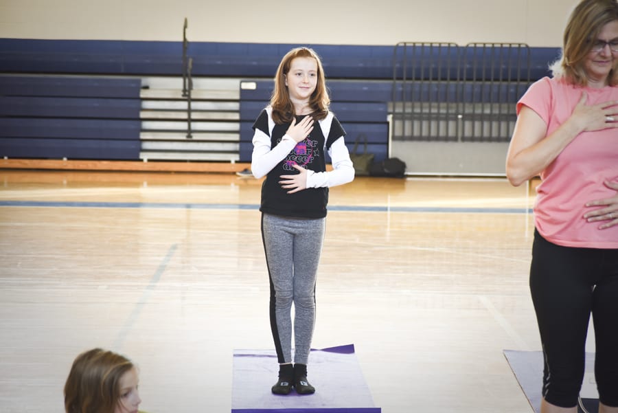 Girl standing on a yoga mat with one hand on her heart beside a woman