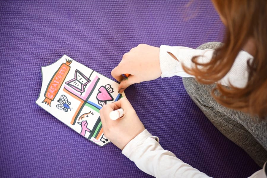 Child coloring a coat of arms with a book, a heart and a butterfly on a purple mat