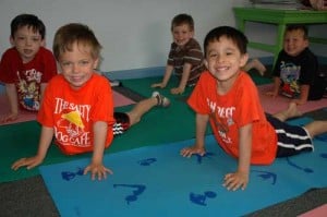 Elementary-age boys smiling on yoga mats during a playful kids yoga session.