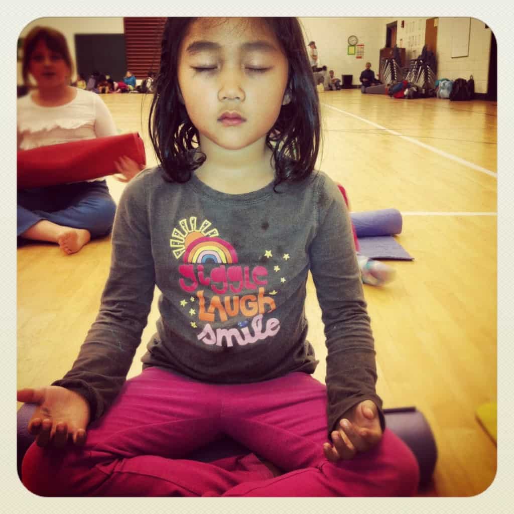 Young child sitting cross-legged with eyes closed, meditating in a gym