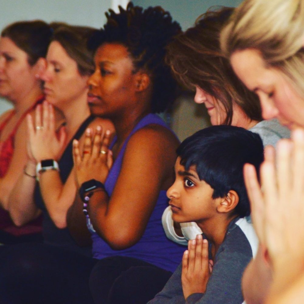 Kids practicing a calming mantra with hands at heart (anjali mudra) in a yoga cla