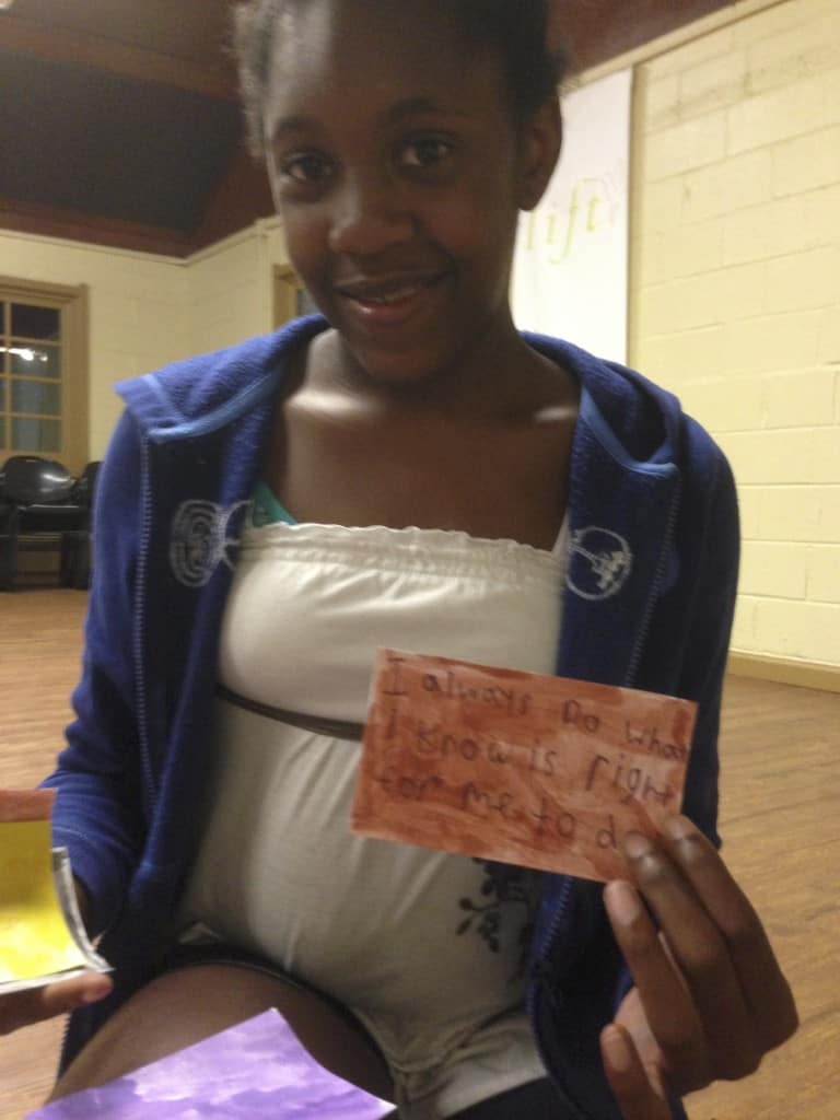 Child showing two finished “I Am” affirmation cards at a table