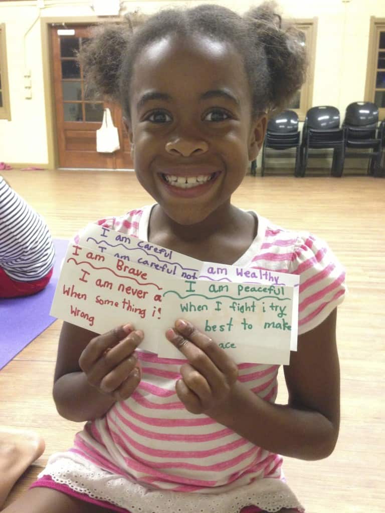 Child displaying finished “I Am” affirmation cards in a kids yoga classroom
